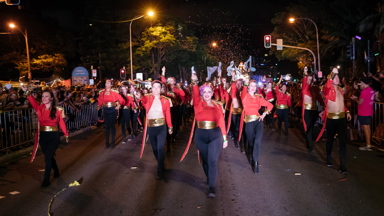 People marching in the street, dressed in red jackets and a gold belt.