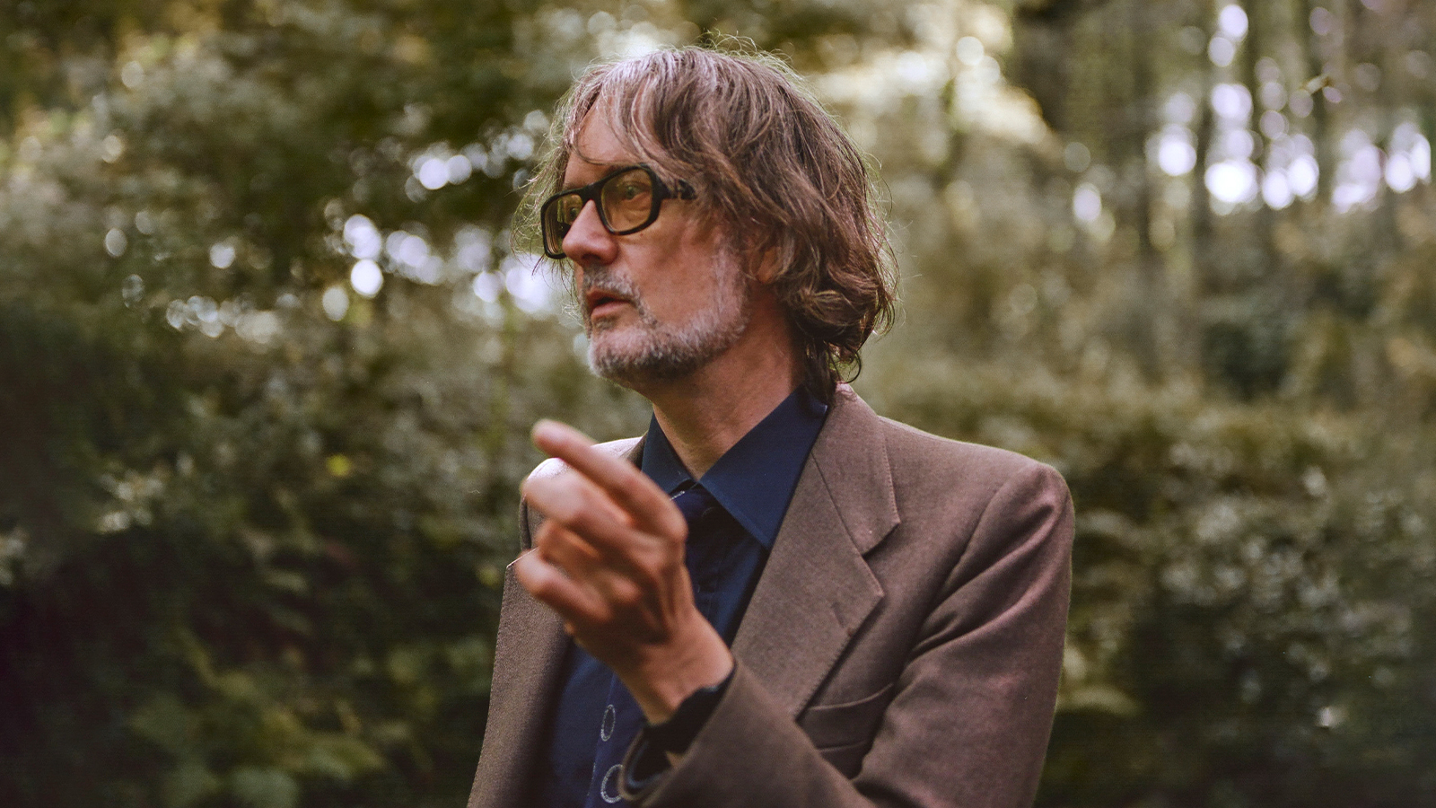 A musician Jarvis Cocker wearing a brown suit jacket with a blue shirt.