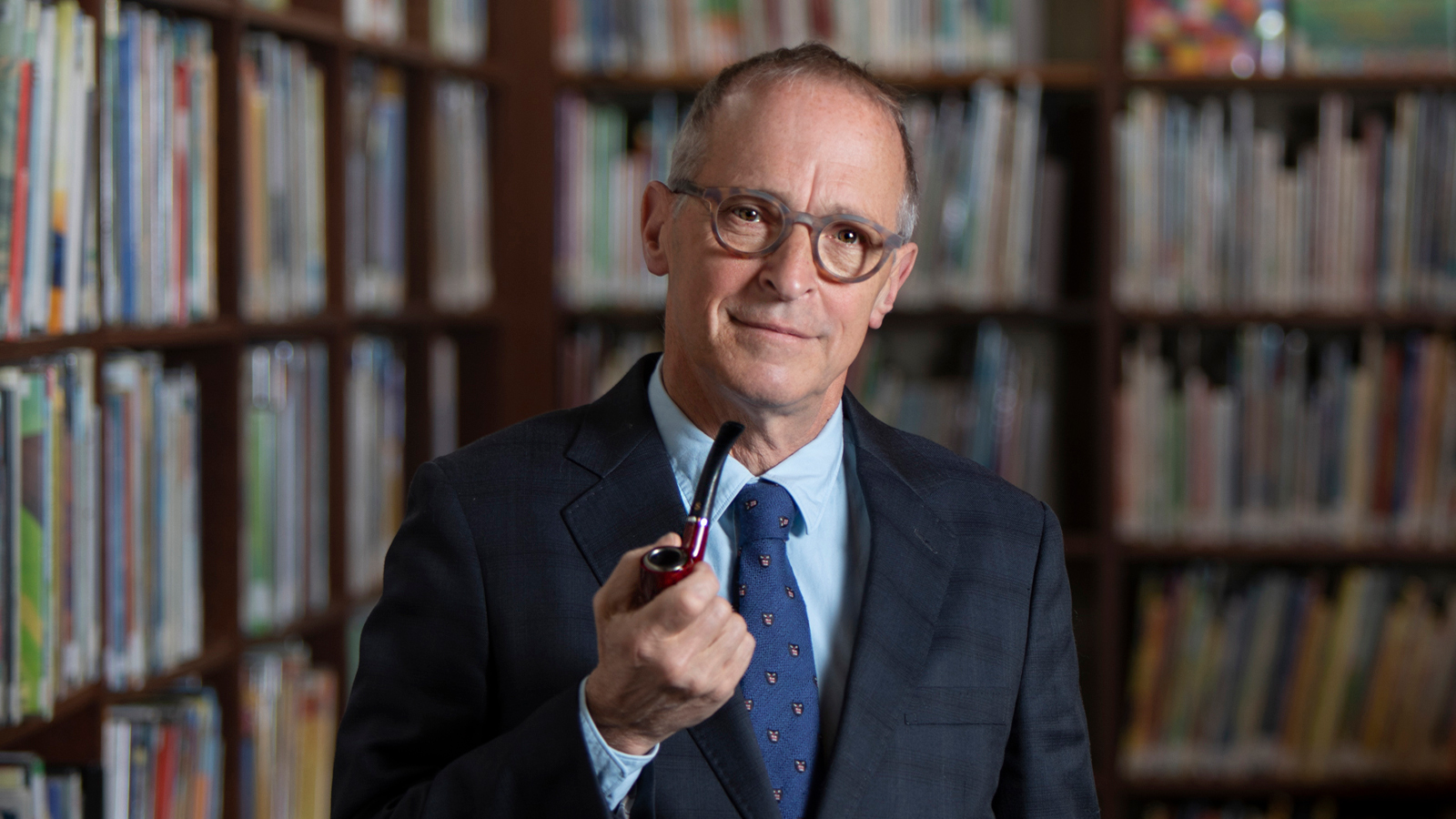 David Sedaris an American humorist in a suit holding a cigar pipe.