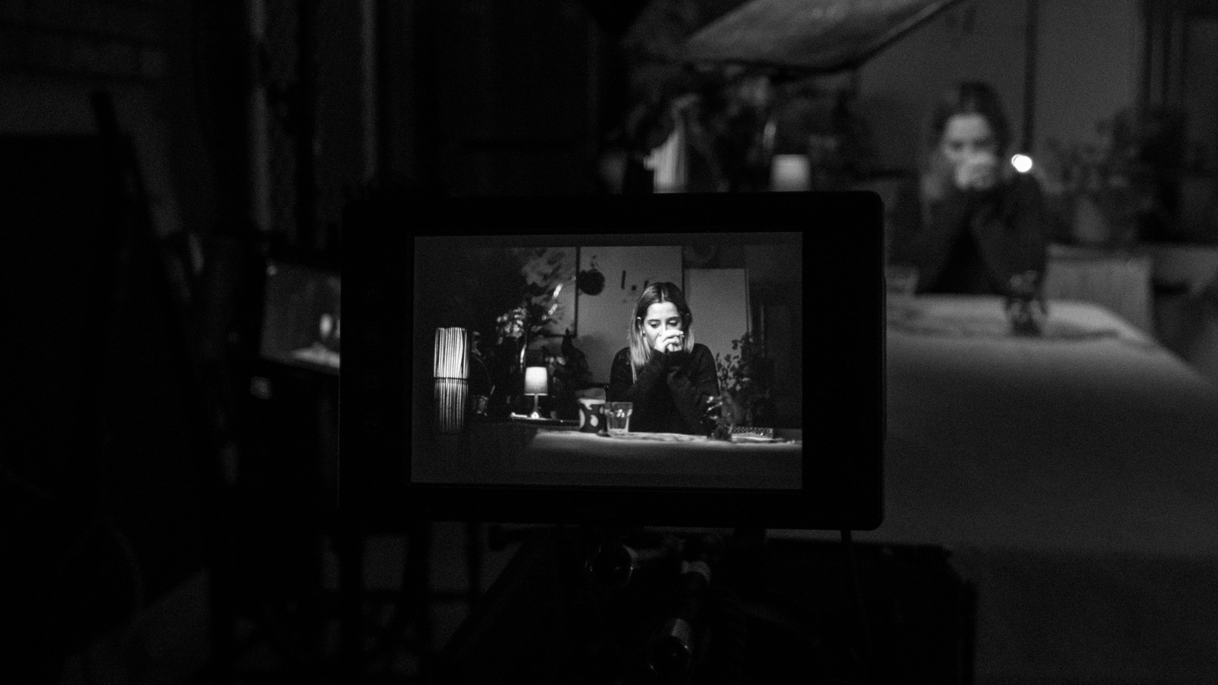 A woman sitting is sitting infront of a camera and resting her face on her hands, captured in black and white.