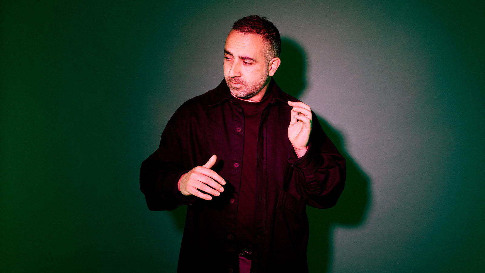 A middle aged man in a black jacket standing in dark studio lighting.