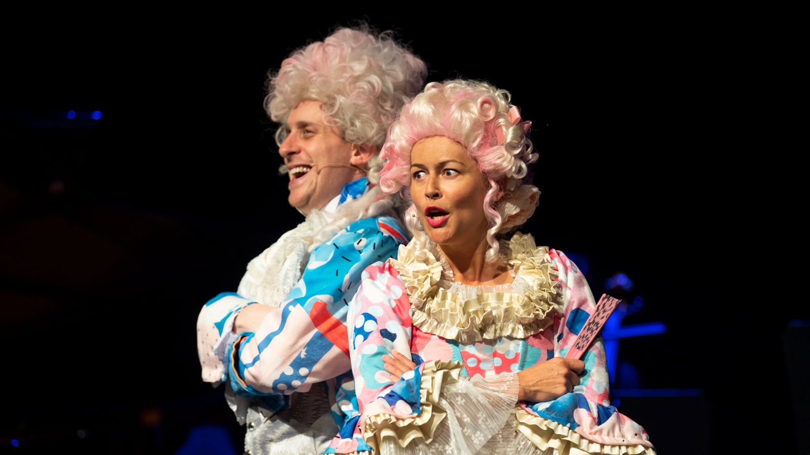 A man and woman dressed up as Mozart and his wife in colourful outfits and big white wigs