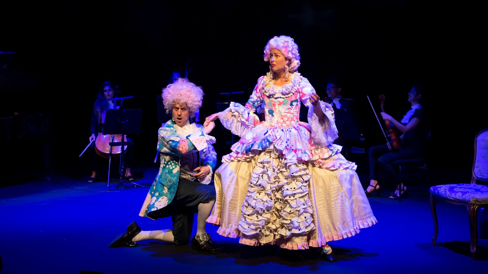 A man and woman dressed up as Mozart and his wife in colourful outfits and big white wigs