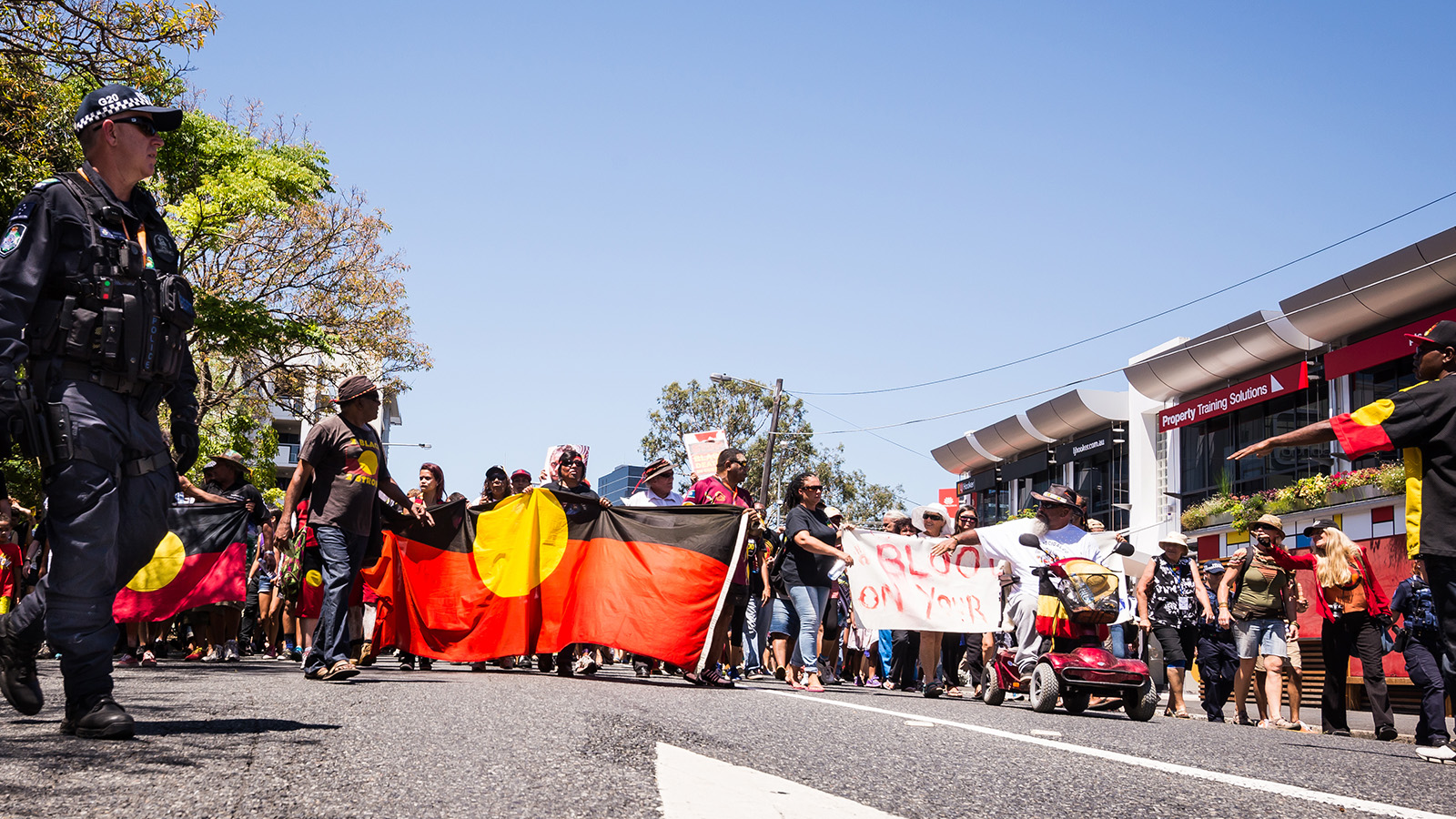 A group of people holding Aboriginal flag protesting on the road.