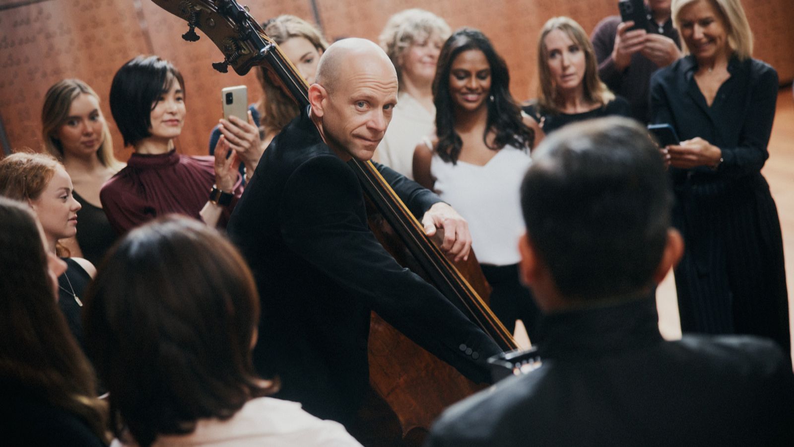 A crowd of people watching a bald man play a bass.