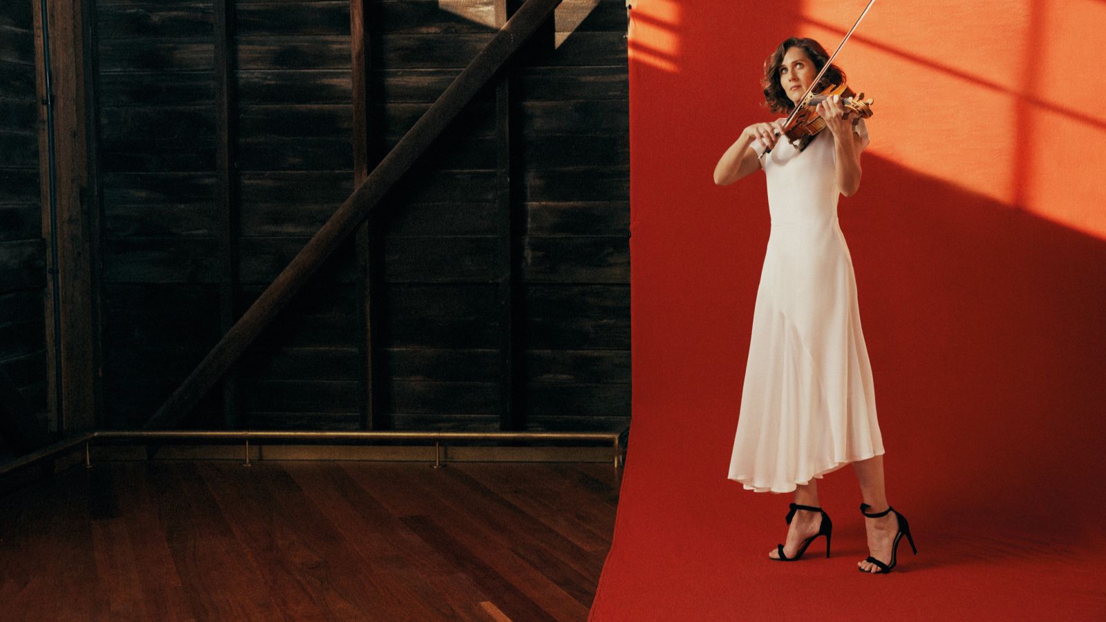 A woman wearing a white dress plays a violin.