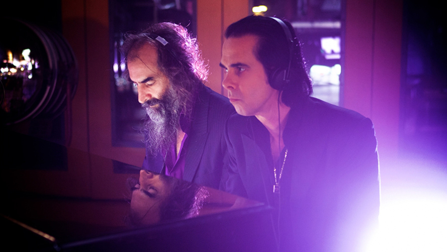 Two men in black shirts in a purple-lit studio with headphones on.
