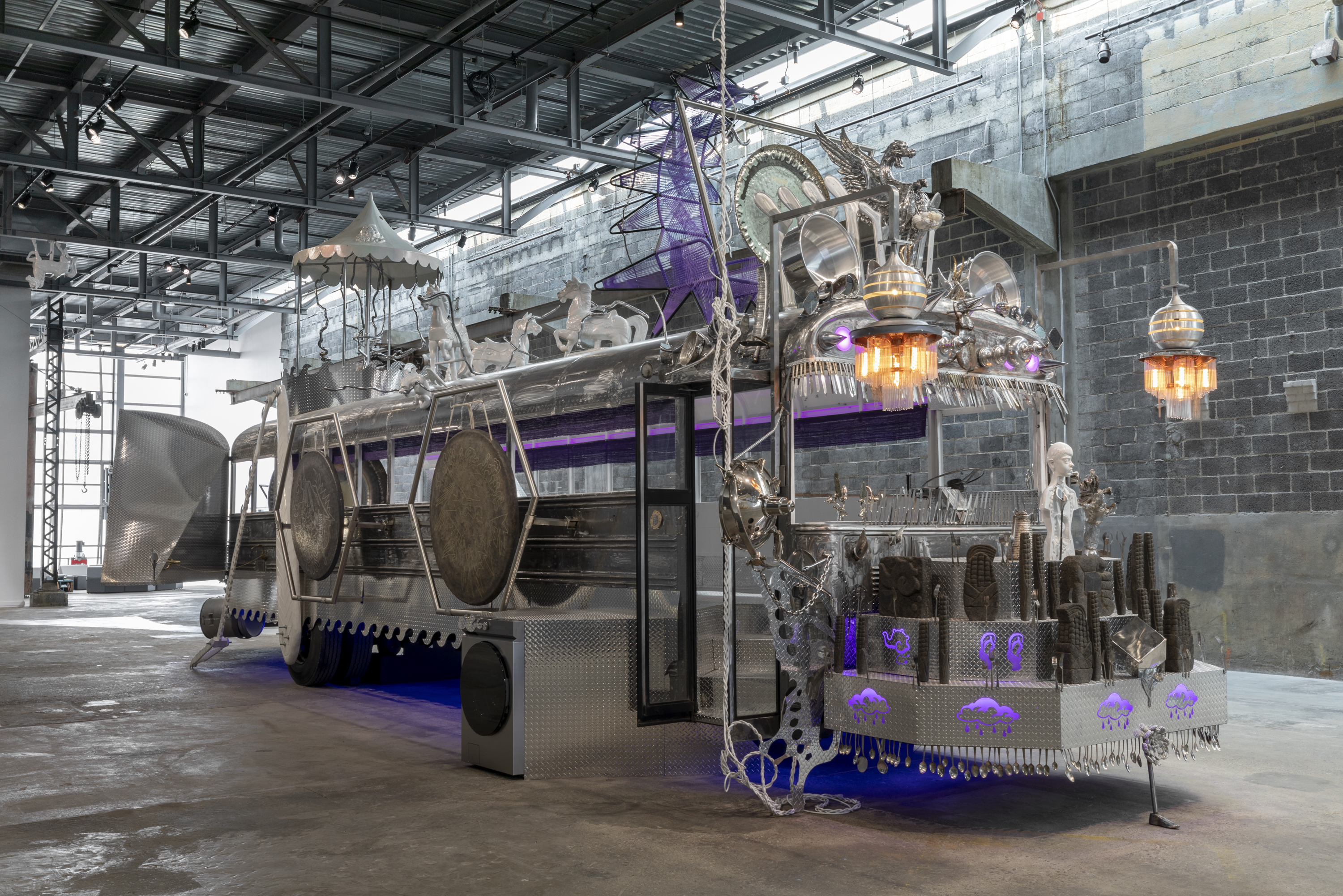 In an industrial envrionment, the steel frame of a bus is decorated with purple and orange lights.