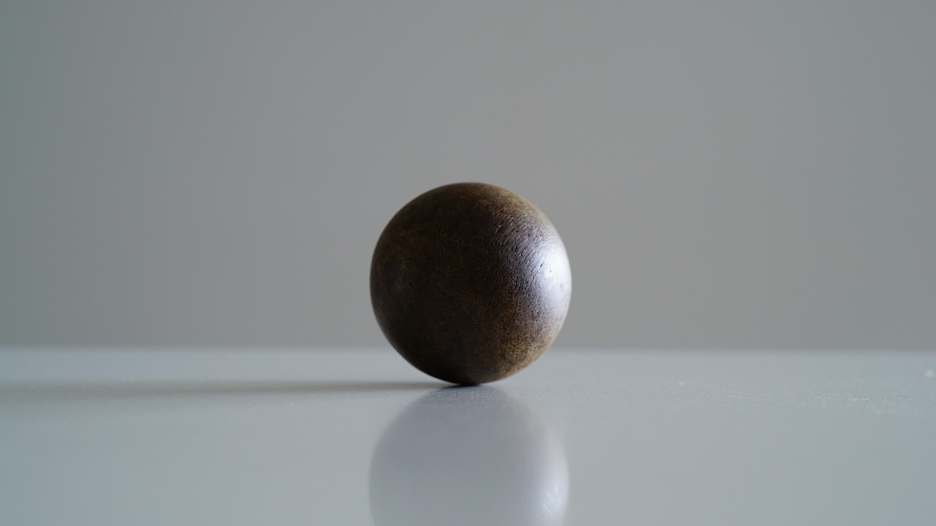 A small brown metal ball sits on a white surface. The background is blured.