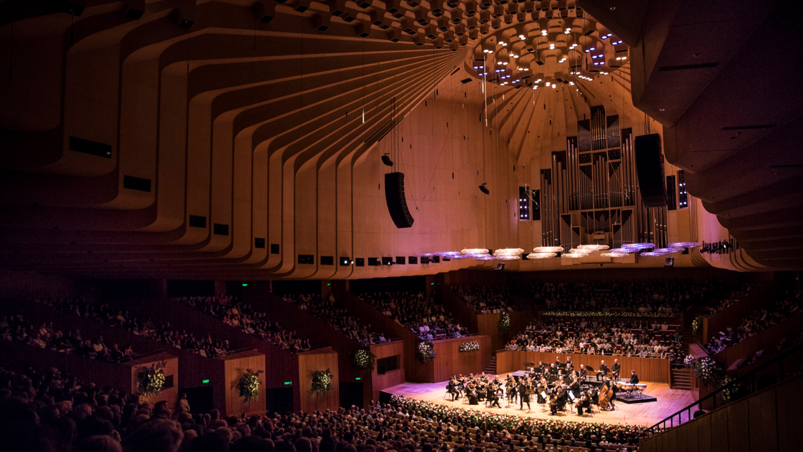 An orchestra performing on stage in the Concert Hall as viewed from the back of the Hall.