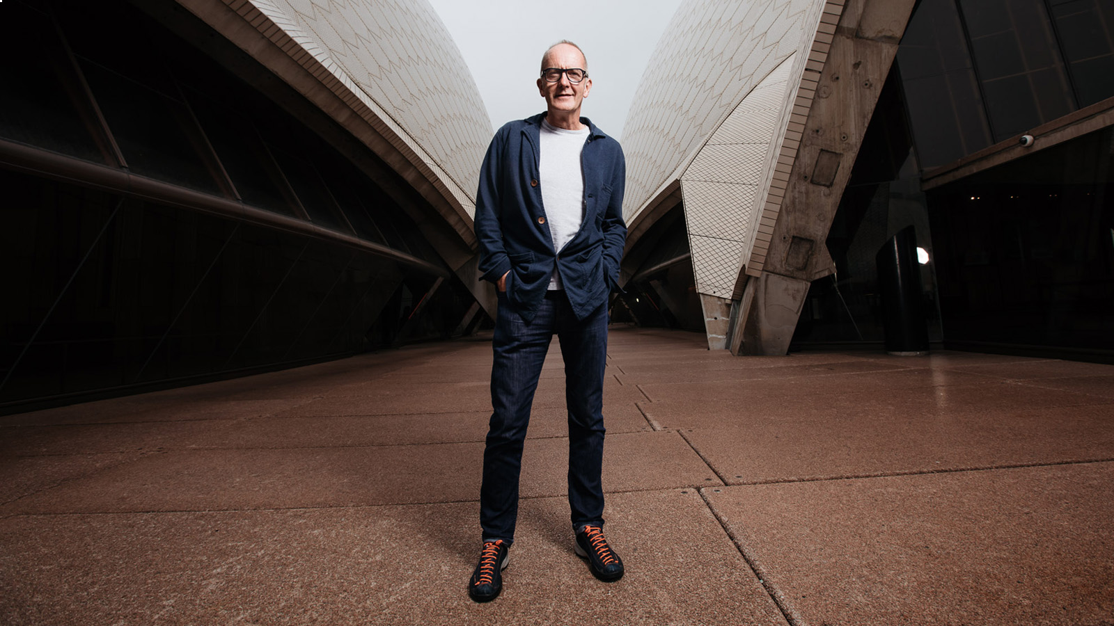 A man in glasses and a suit standing outside the Sydney Opera House.