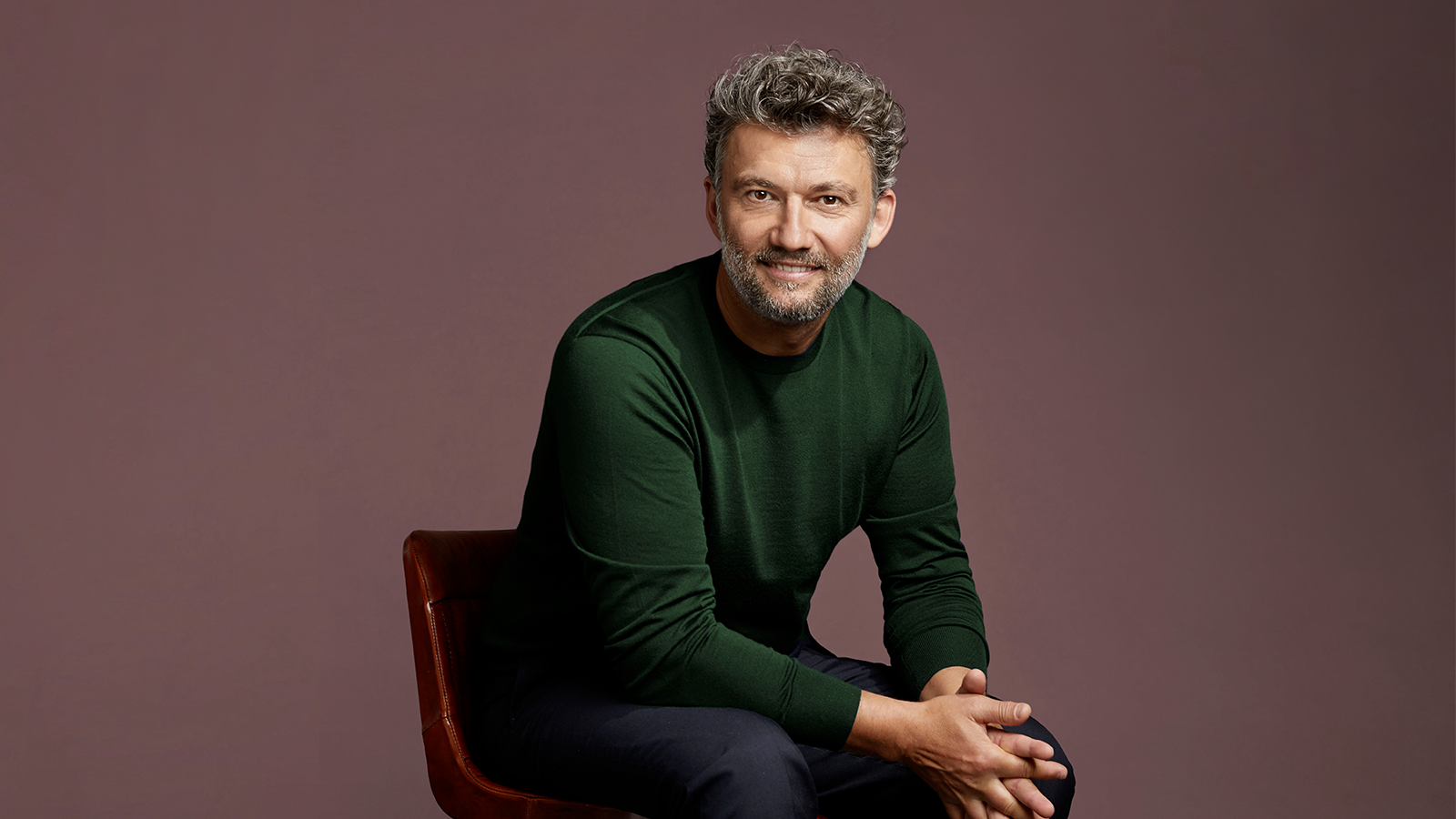 A man with grey hairs in green sweater sitting on the chair.