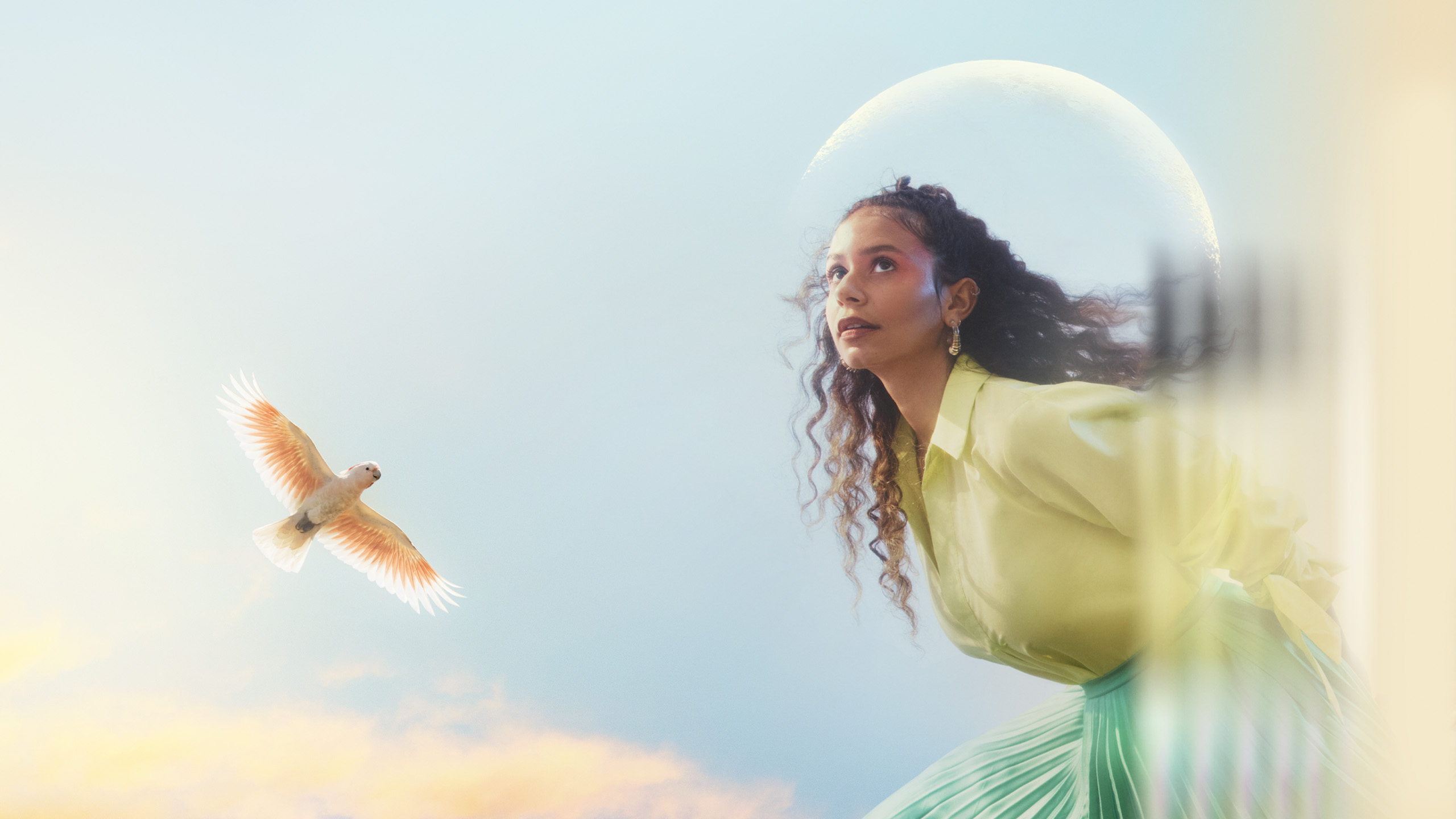 A performer wears a light green blouse with pink eyeshadow looks off camera, the moon and a bird is seen behind her