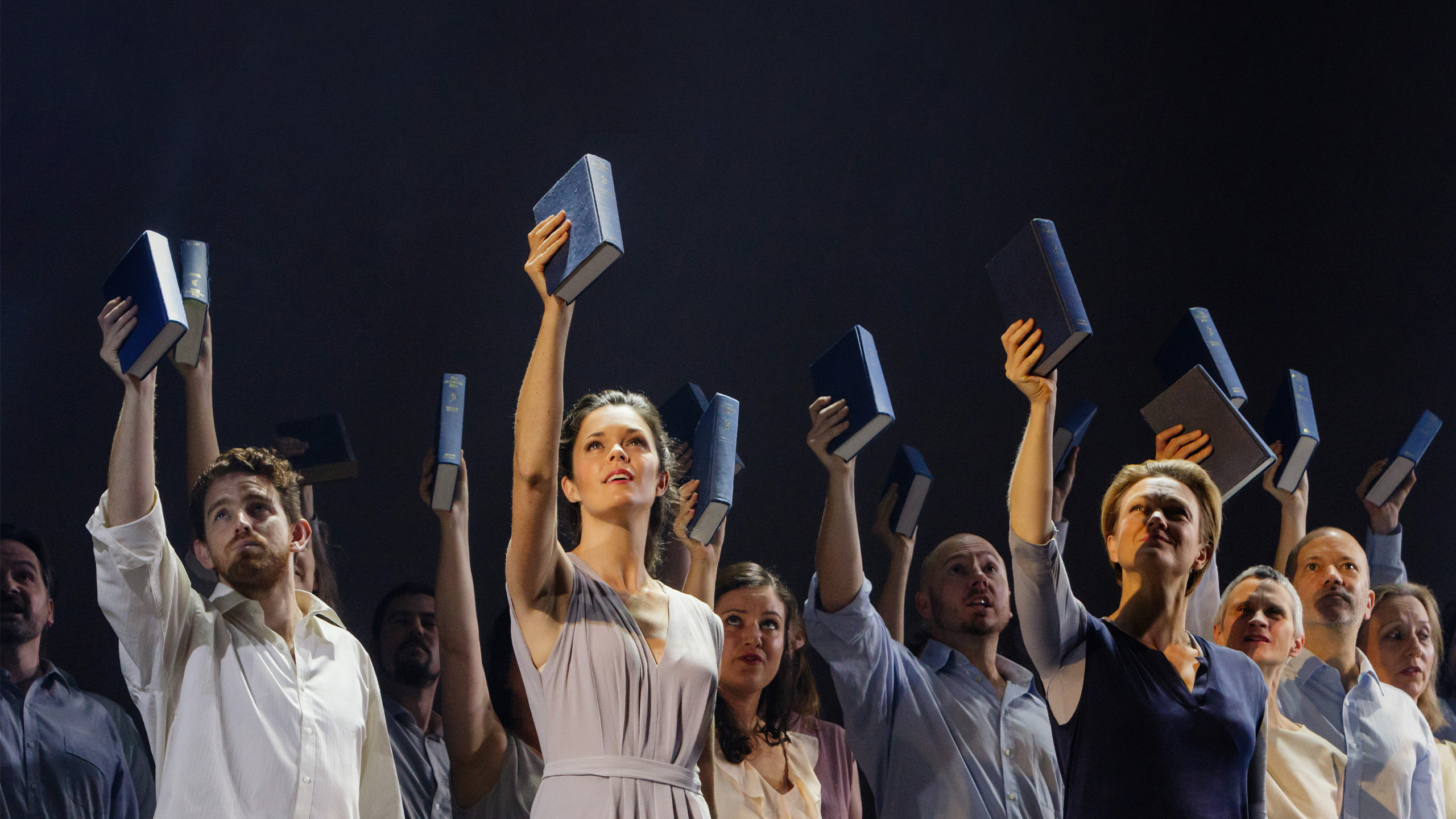 The cast wears neutral outfits, all holding up a book in their right hand