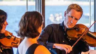 Three violin players stand playing the violin in the Sydney Opera House Utzon Room