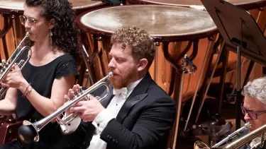 Three trumpet players of the Sydney Symphony Orchestra play the trumpet in front of the Timpani and percussion section
