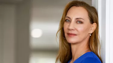 Woman wearing blue dress, leaning against wall with a reflective expression.