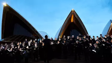 An orchestra playing outside the Sydney opera house at dusk.