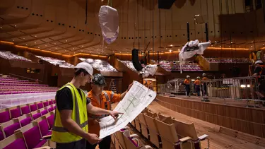 Two builders holding a planning map in the Concert Hall.