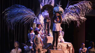 A group of children performing on the stage, holding a big hand made bird.