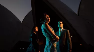 A man in a suit and two women in dresses standing outside the Sydney Opera House.