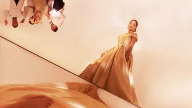 Woman in gold ballgown stands away from other partygoers
