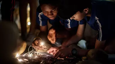 Two young boys crouched over a project featuring bright lights.