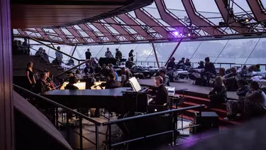 A group of people sleeping on mattresses inside a building with musicians playing instruments.