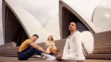 Three individuals sitting outside on the stairs of Sydney opera house.