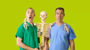 Two men in medical attire studying a skeleton in a lab setting.