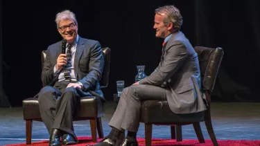 Two middle age men wearing suit, having a debate on the stage.