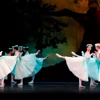 Two groups of six ballerinas on stage, in arabesque, wearing long white tutus and flower crowns.