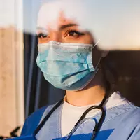 A doctor wearing a mask and a statoscope looking through a window.