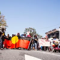 A group of people holding Aboriginal flag protesting on the road.