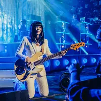 Woman with long dark hair knees while playing bass guitar on stage