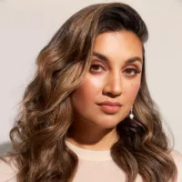 A headshot of a woman with flowing wavy brown hair dressed in a beige top.