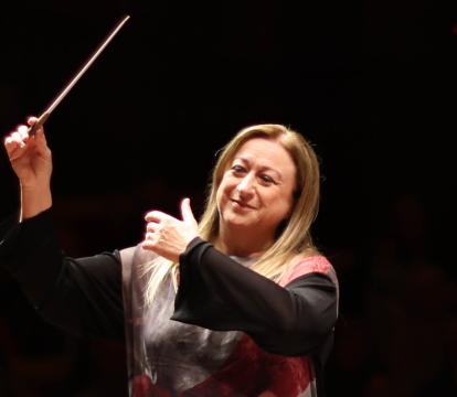 Simone Young conducts with baton in the hand in front of an orchestra