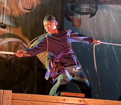 An Asian man pulling on a rope wearing with rain effects in the background