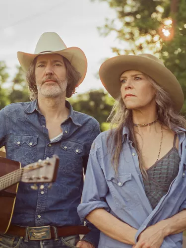 A man holding a guitar and woman both in cowboy hats look pensive away from the camera exuding a country music vibe.