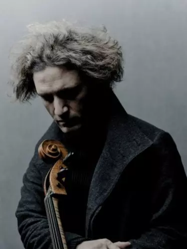 A 40-50 year old man with medium length grey hair wearing a coat looks down at the top of a string instrument.