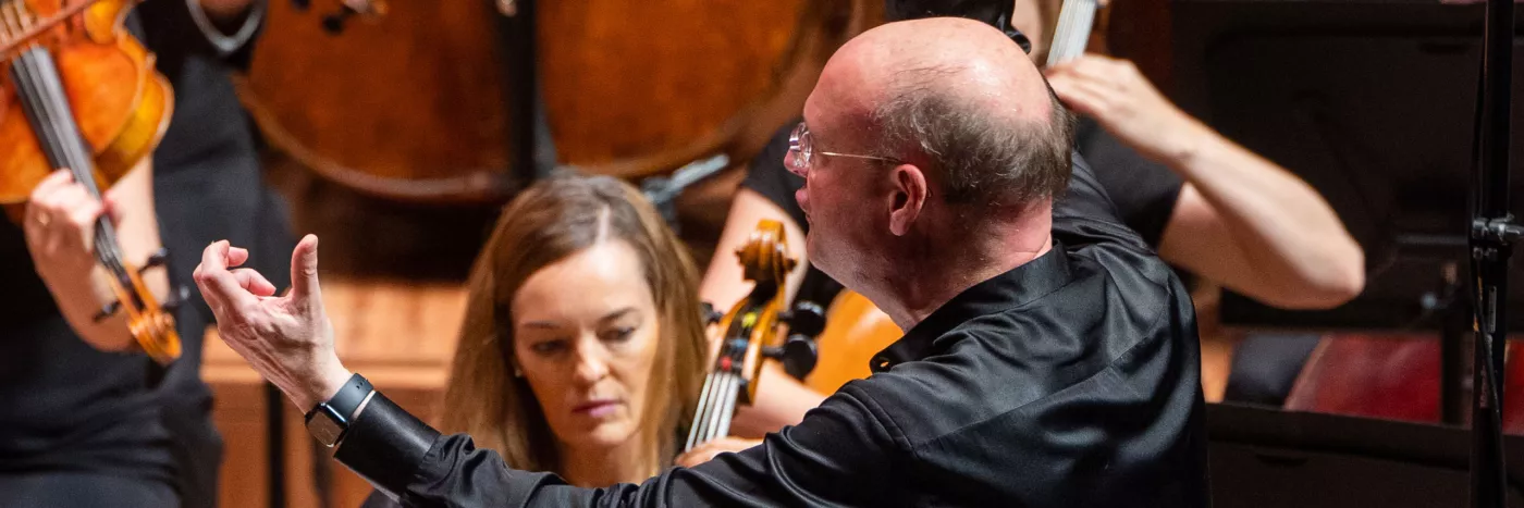 Stephen Layton conducts an Orchestra with arms outstretched