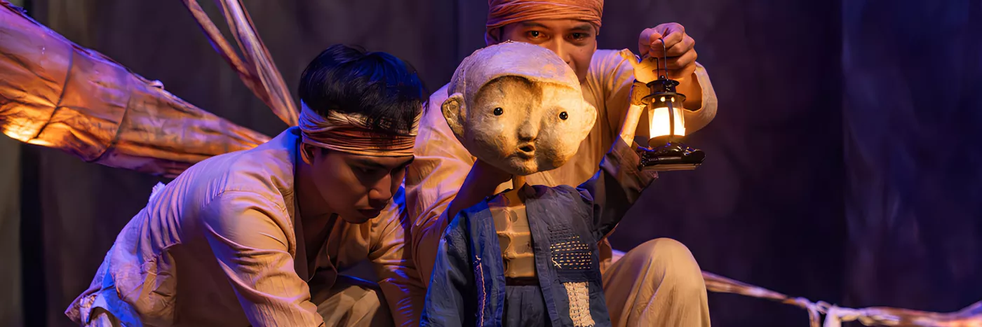 Two men hold a beautifully crafted puppet of a young child holding a lantern.