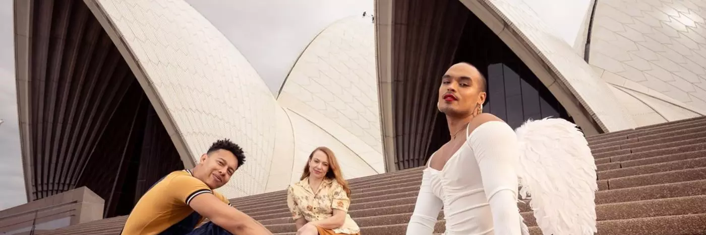 Three individuals sitting outside on the stairs of Sydney opera house.