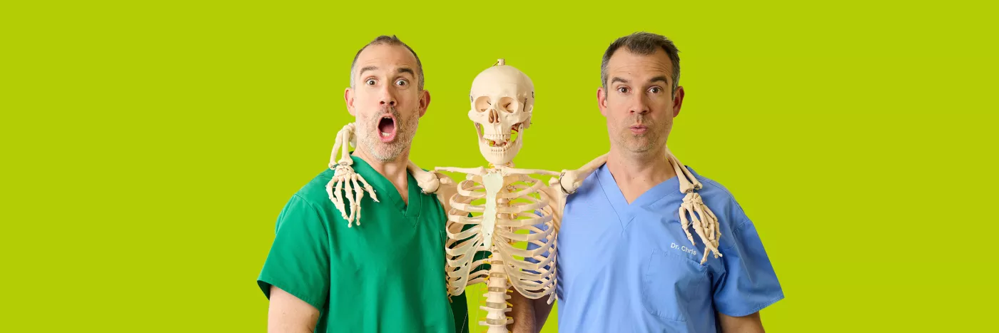 Two men in medical attire studying a skeleton in a lab setting.