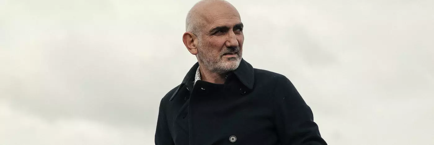 A man with grey hair in a black coat standing outside.