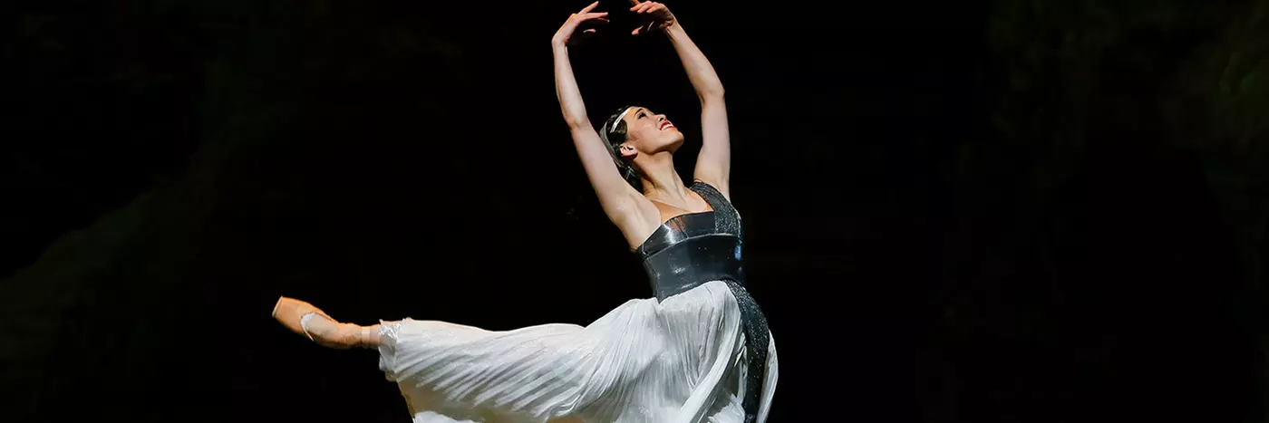 A woman in a white dress leaping with her hands above her head.