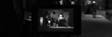 A woman sitting is sitting infront of a camera and resting her face on her hands, captured in black and white.