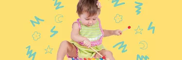 A baby sitting on the floor playing a coloured toy xylophone.