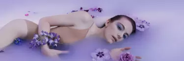 An opera Adriana Lecouvreur laying in purple pool of water with flowers around her.