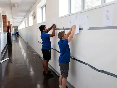 Children putting up posters in a hallway at school.
